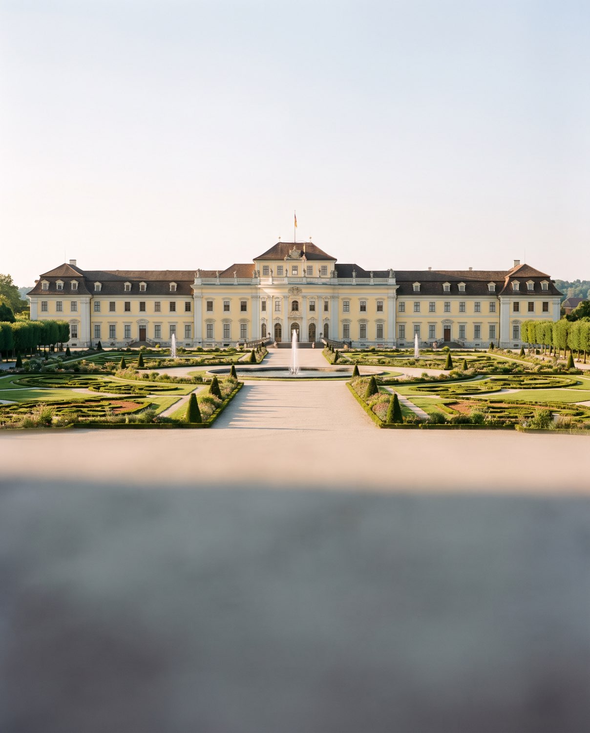 Barockschloss mit langer heller Fassade hinter einem Garten mit Springbrunnen