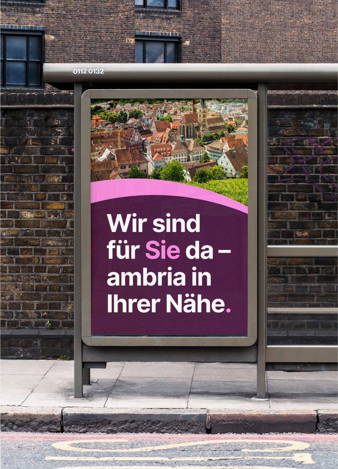 Ein ambria-Plakat im Schaukasten einer Bushaltestelle, dahinter eine Backsteinwand